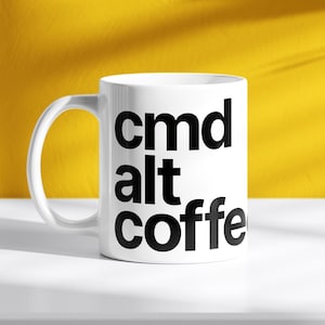 May include: White ceramic coffee mug with black text that reads "cmd alt coffee".