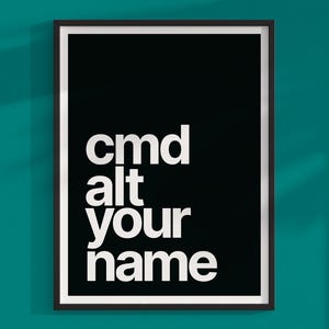 Puede incluir: Impresión artística enmarcada con el texto "cmd alt your name" en blanco sobre fondo negro. El marco negro y el borde blanco resaltan el mensaje. El póster está colgado en una pared turquesa, creando un contraste llamativo.