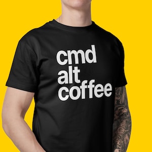 May include: Black t-shirt with the words "cmd alt coffee" in white, stacked vertically. The shirt is on a person against a yellow background. The person has a tattoo on their arm.