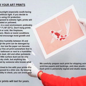 May include: A person wearing a red sweater and white gloves holds a framed art print. The print features a koi fish design in red and white on a peach background. Text on the left provides care instructions for art prints.