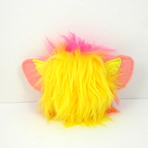 May include: A yellow and pink fuzzy toy with pink ears. The toy has a long, yellow, fluffy mane.