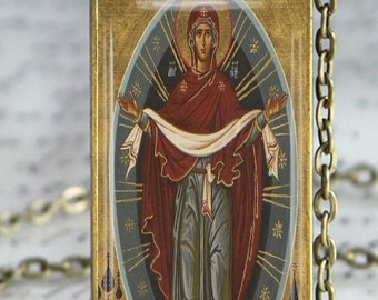 May include: A gold pendant necklace with a rectangular glass charm featuring a religious icon of the Virgin Mary. The icon is painted in a traditional style with a red and blue robe and a white veil. The background is gold with a blue oval and stars.