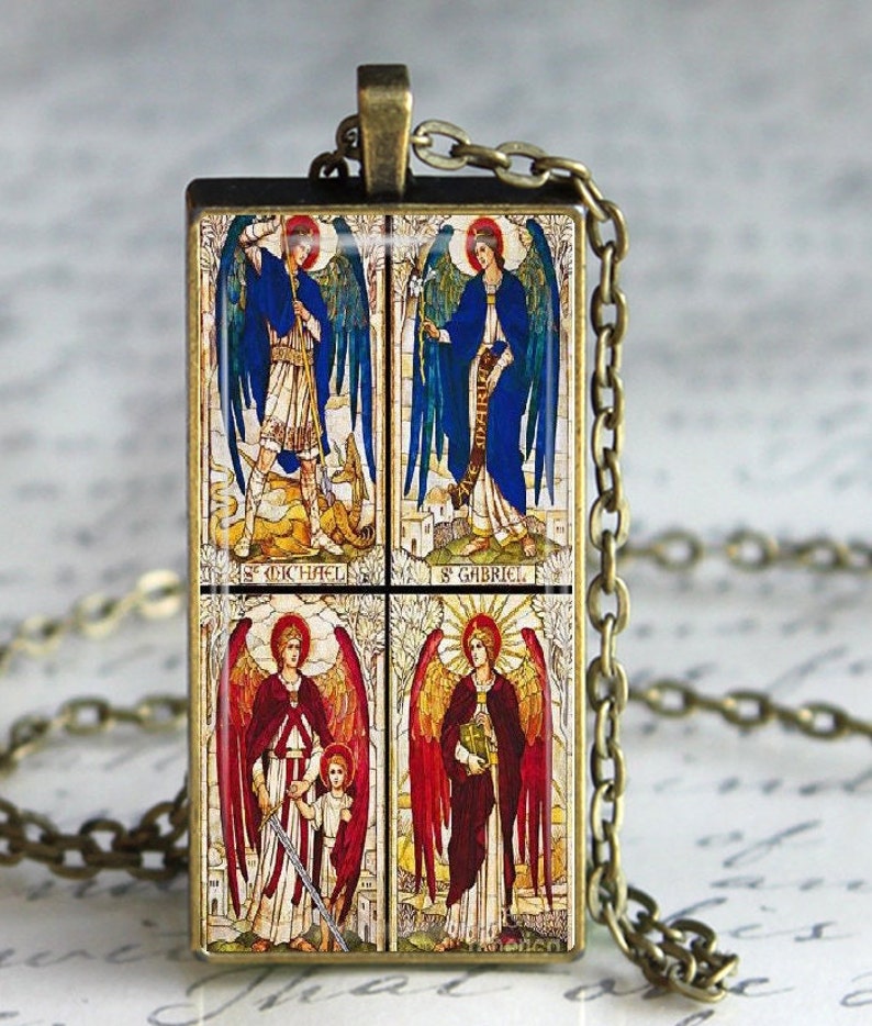 May include: A gold pendant necklace with a rectangular glass charm featuring four colorful images of angels. The charm has the names "St. Michael", "St. Gabriel", "St. Raphael", and "St. Uriel" written below each image.