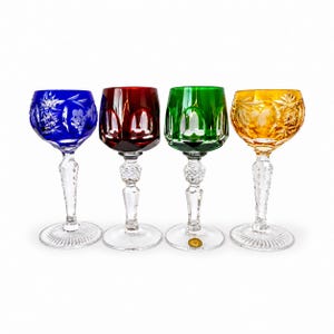 May include: A set of four crystal wine glasses featuring coloured bowls in blue, red, green, and amber. Each glass has a clear, faceted stem and a round base. The blue and amber bowls display intricate star and leaf cut patterns.