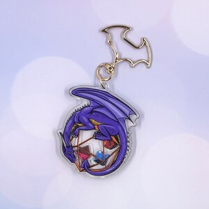 May include: Purple dragon keychain with a gold metal clasp. The dragon is curled around a clear, multi-sided die with different colored dice inside.
