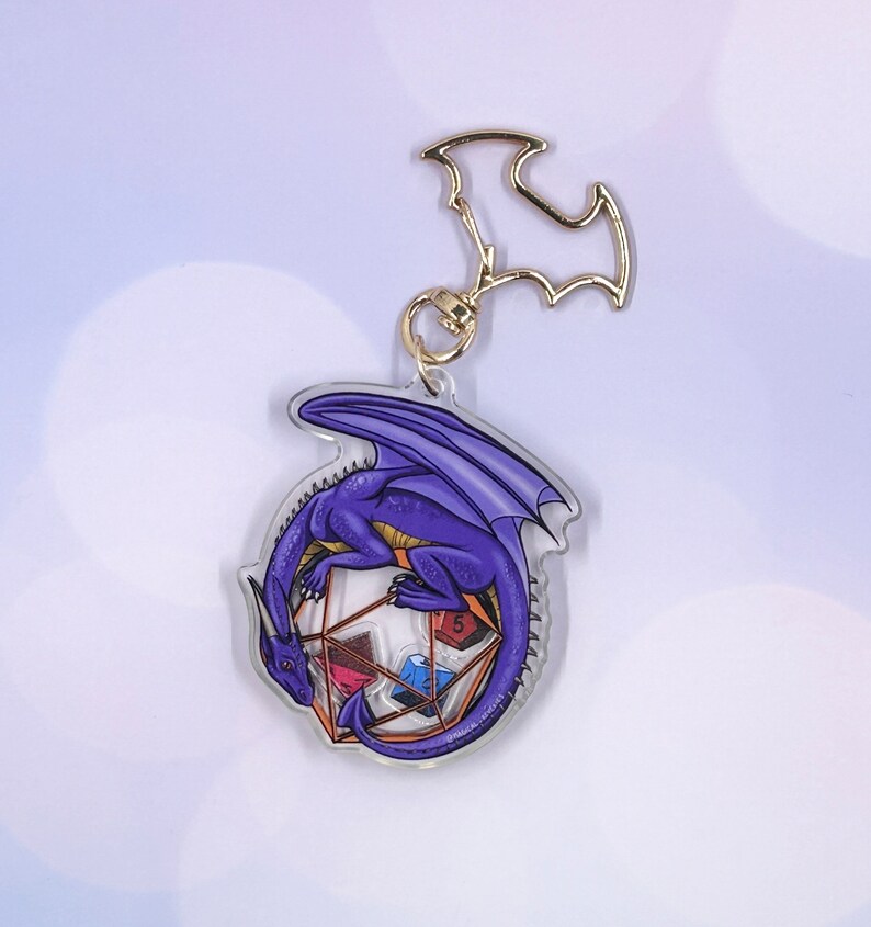 May include: Purple dragon keychain with a gold metal clasp. The dragon is curled around a clear, multi-sided die with different colored dice inside.