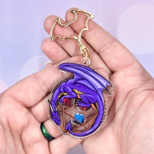 May include: Purple dragon keychain with gold accents, curled around a clear, multi-sided dice with red, blue, and green dice inside.
