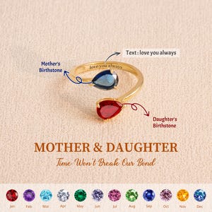 Op de afbeelding: Een goudkleurige ring met twee druppelvormige edelstenen, een blauwe en een rode. De ring is gegraveerd met "love you always". De tekst "Mother & Daughter" en "Time Won't Break Our Bond" is ook zichtbaar.