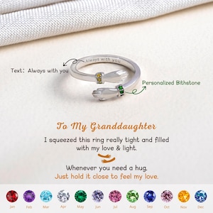 May include: A silver-colored ring with two hands embracing. The ring has a personalized birthstone and the text "Always with you". The ring is designed to be a hug ring.