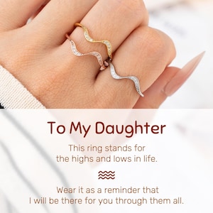 May include: Three wave-shaped rings in gold, rose gold, and silver, each adorned with small, sparkling stones. The rings are worn on a hand. Text at the bottom reads "To My Daughter" and a message about life's highs and lows.
