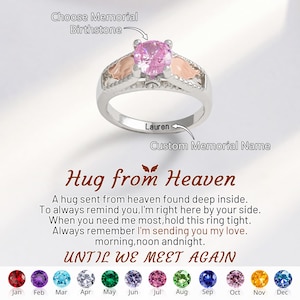 Könnte beinhalten: Ein silberner Ring mit einem großen rosa Edelstein in der Mitte und kleinen goldfarbenen Flügeln auf jeder Seite. Der Ring trägt den Namen "Lauren". Der Text "Hug from Heaven" und "Until We Meet Again" sind ebenfalls sichtbar.
