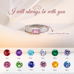 Può includere: Un anello d'argento con una gemma rosa rettangolare al centro, affiancata da pietre chiare più piccole. L'anello è inciso con "Brandi 1956-2020". Il testo "I will always be with you" è sopra l'anello. Sotto, gemme colorate che rappresentano i mesi.