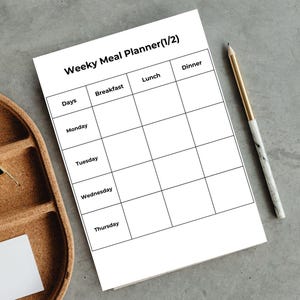 May include: A white weekly meal planner with the title "Weeky Meal Planner (1/2)" and a grid for daily meal planning. A gold and marble pen rests on the right side. A wooden tray is on the left side.