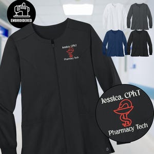 Puede incluir: Chaqueta de uniforme médico negra con cremallera y mangas largas. Presenta un símbolo de farmacia rojo bordado y el texto "Jessica, CPhT Pharmacy Tech". También se muestran chaquetas adicionales en blanco, gris, azul marino y negro.