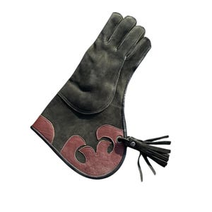 May include: A dark green leather glove with a decorative maroon accent. The glove features a stylized design on the cuff and a black leather tassel. The glove is designed to protect the hand and forearm.