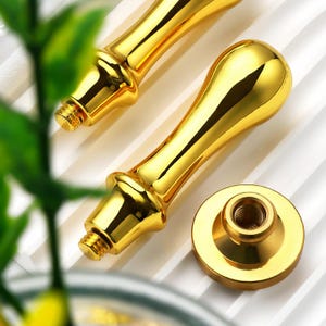 Puede incluir: Primer plano de dos sellos de lacre dorados y un cabezal de sello separado. Los sellos tienen un diseño clásico con un mango redondeado y una base roscada. El cabezal del sello es redondo con un centro roscado.