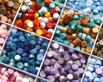 May include: A variety of colorful wax seal beads in a clear divided container. The beads are in shades of red, orange, yellow, white, blue, green, and purple. The hexagonal beads are for crafts and stationery.