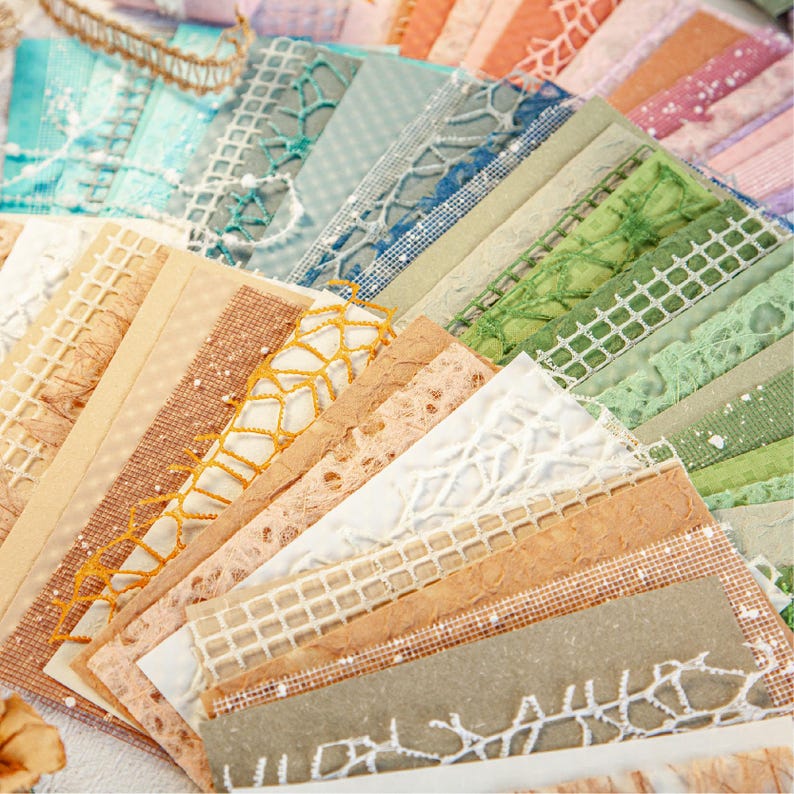 May include: A collection of decorative paper sheets in various colors and textures. The papers feature lace, netting, and patterned designs in shades of blue, green, orange, and beige. Ideal for scrapbooking, card making, or other craft projects.