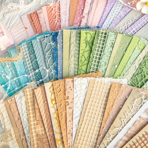 May include: A collection of textured paper sheets in various colors, including blue, green, beige, and pink. The papers feature embossed patterns like lattice, floral, and geometric designs. Ideal for scrapbooking, card making, and other paper crafts.
