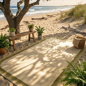 K&ouml;nnte beinhalten: Ein rechteckiger beiger Teppich mit gr&uuml;nem Rand liegt an einem Sandstrand. Eine Holzbank mit Topfpflanzen steht unter einem gro&szlig;en Baum. Ein Weidenkorb mit einer Decke und weiteren Pflanzen befindet sich in der N&auml;he. Das Meer ist im Hintergrund zu sehen.