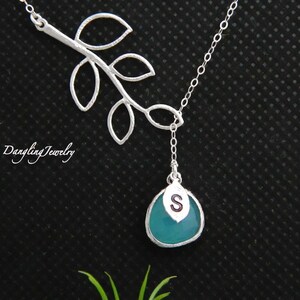 Könnte beinhalten: Eine silberne Halskette mit einem filigranen Ast-Design und einem türkisfarbenen Tropfen-Anhänger mit einem silbernen Buchstaben 'S'-Anhänger. Dangling Jewelry.