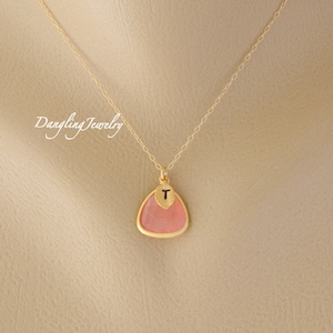 May include: A gold chain necklace with a pink triangle pendant. The pendant has a gold letter "T" on the front.