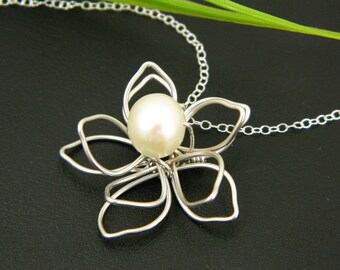 May include: A silver wire flower pendant necklace with a white pearl in the center.