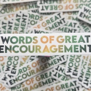 May include: White sticker with the words "WORDS OF GREAT ENCOURAGEMENT" in green, orange, and black. The sticker is surrounded by other stickers with the same text. The stickers are rectangular with rounded edges.