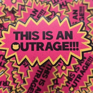May include: A collection of pink stickers with a yellow jagged border. The stickers have the phrase "THIS IS AN OUTRAGE!!!" in black text, with a small cat face icon. The stickers are scattered.