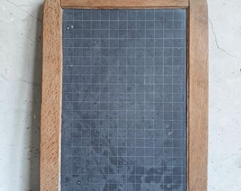 May include: A rectangular slate writing board framed in light brown wood. The dark grey surface features a white grid pattern. A small hole is centred at the top of the frame. The bottom frame is stamped with the text No 3 and a small star symbol.