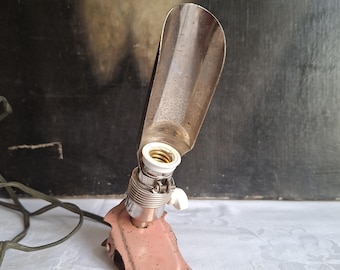 May include: A vintage clip-on lamp fixture featuring a dusty pink metal base with a worn finish and a silver-toned metal reflector shade. The lamp includes a standard light bulb socket with a white plastic switch and a long electrical cord.