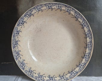 May include: A round ceramic bowl with a cream-colored base and a speckled finish. The rim features a repeating blue floral pattern consisting of stylized petals and dots arranged in a symmetrical border around the entire circumference.