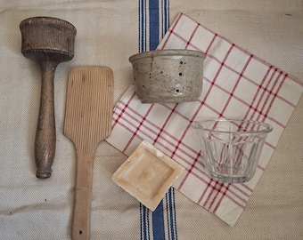 May include: A collection of kitchen tools including a dark wooden mallet, a light wooden ridged paddle, a speckled ceramic bowl with small drainage holes, a square off-white ceramic tile, and a clear glass ramekin with vertical fluted sides.