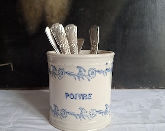 May include: A cylindrical ceramic canister with an off-white glaze and blue floral bands at the top and bottom. The word POIVRE is printed in blue on the front. Several silver-toned metal spoons with ornate handles are placed inside the container.