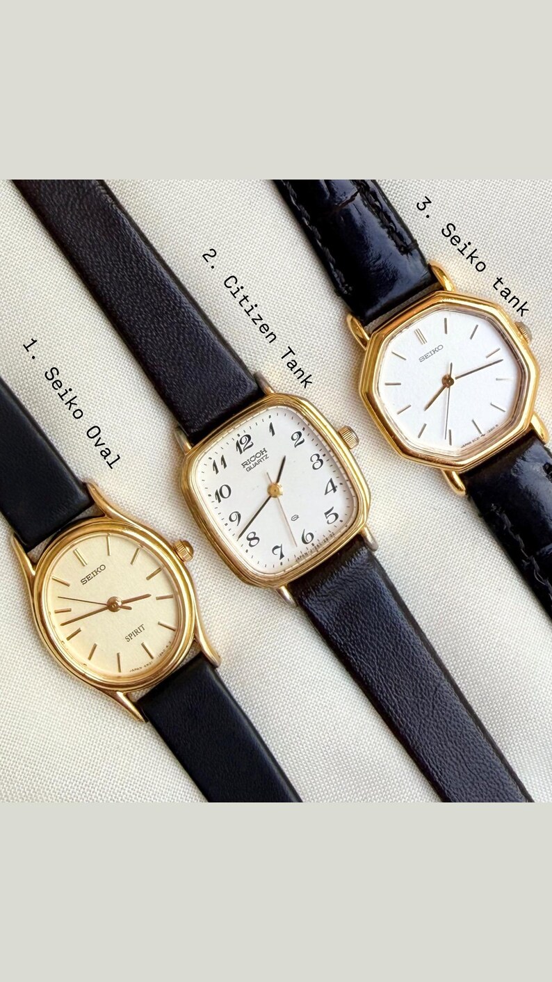 May include: Three vintage gold-toned wristwatches with black leather bands. The watches have white or cream-colored faces with black numerals and hands. The first watch is a Seiko Oval, the second is a Citizen Tank, and the third is a Seiko Tank.