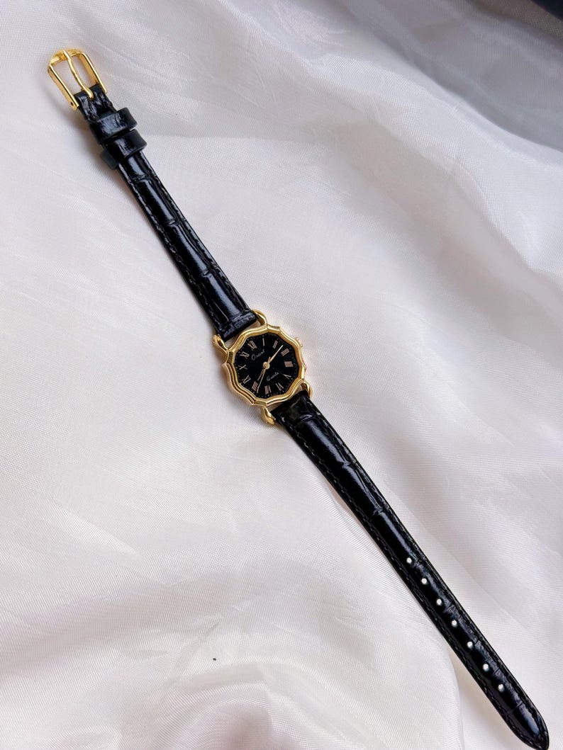May include: A black wristwatch with a gold octagonal face and black leather strap. The watch has Roman numeral hour markers and a gold buckle. The strap is approximately 1.3 cm wide.