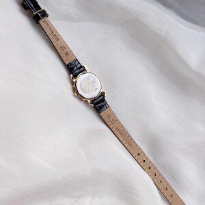 May include: A gold wristwatch with a black leather strap. The watch face is octagonal. The strap is marked "STAIER" and "GENUINE LEATHER". The watch is shown on a white, textured background.
