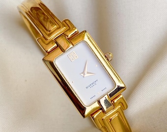 May include: A gold-toned Givenchy Paris watch with a rectangular white face. The watch features a gold band and a small crown. The face displays the Givenchy logo and the words "SWISS MADE".