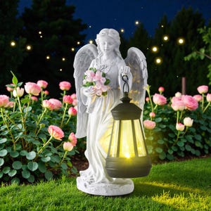Könnte beinhalten: Eine weiße Engelsstatue, die einen Strauß rosa Blumen und eine schwarze Laterne mit gelbem Licht hält. Die Statue befindet sich in einem Garten mit rosa Rosen und einem dunklen Nachthimmel mit funkelnden Lichtern.