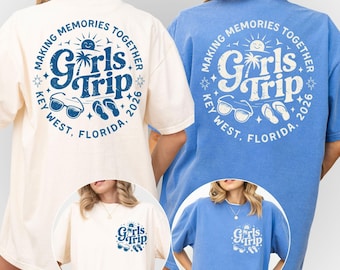 May include: Two short-sleeved t-shirts in ivory and blue, each featuring a large circular graphic on the back and a smaller version on the front left chest. The design includes the text "Making Memories Together", "Girls Trip", "Key West, Florida, 2026", a sun, palm tree, sunglasses, and flip-flops.