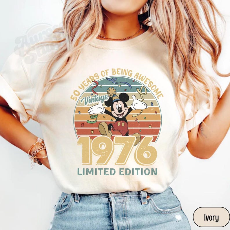 Puede incluir: Camiseta de color marfil con un dise&ntilde;o vintage de Mickey Mouse. El gr&aacute;fico incluye el texto "50 Years of Being Awesome", "Vintage", "1976" y "Limited Edition". Mickey se muestra celebrando dentro de un dise&ntilde;o circular.