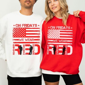 Może przedstawiać: Czerwone i białe bluzy z napisem "ON FRIDAYS WE WEAR RED" oraz wzorem amerykańskiej flagi. Projekt zawiera sylwetki żołnierzy. Bluzy to patriotyczne oświadczenie.