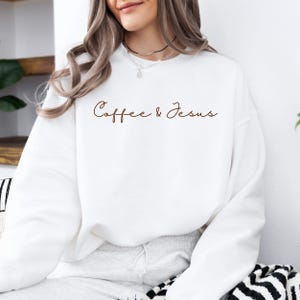 Puede incluir: Sudadera blanca con la frase "Coffee & Jesus" en escritura marr&oacute;n. La sudadera es de cuello redondo y parece estar hecha de un material suave. La est&eacute;tica general es informal y c&oacute;moda.