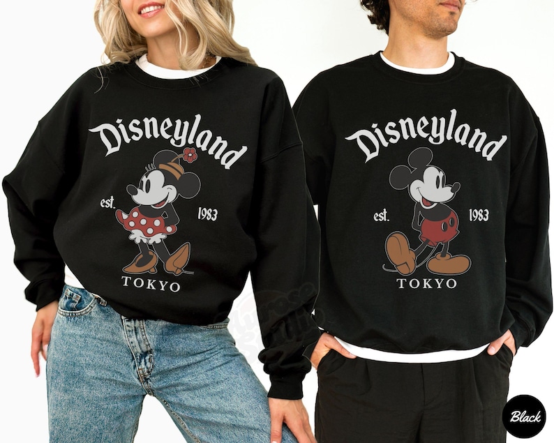 Puede incluir: Sudaderas negras con ribete blanco con el logotipo de Disneyland y gr&aacute;ficos de Mickey y Minnie Mouse. Las sudaderas tienen el texto "est. 1983 TOKYO". Llevadas por dos personas.