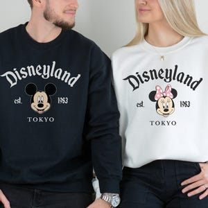 May include: Black and white sweatshirts featuring the Disneyland logo, Mickey Mouse and Minnie Mouse. The sweatshirts have the text "Disneyland est. 1983 TOKYO". The Mickey Mouse sweatshirt is black, and the Minnie Mouse sweatshirt is white.