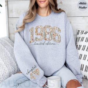 May include: Athletic heather gray sweatshirt with the year "1986" in a floral design. The words "limited edition" are below the year. The left sleeve has the word "chapter" and a floral heart design.