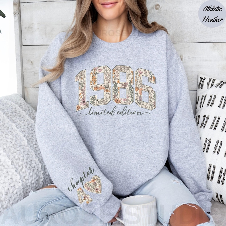 May include: Athletic heather gray sweatshirt with the year "1986" in a floral design. The words "limited edition" are below the year. The left sleeve has the word "chapter" and a floral heart design.