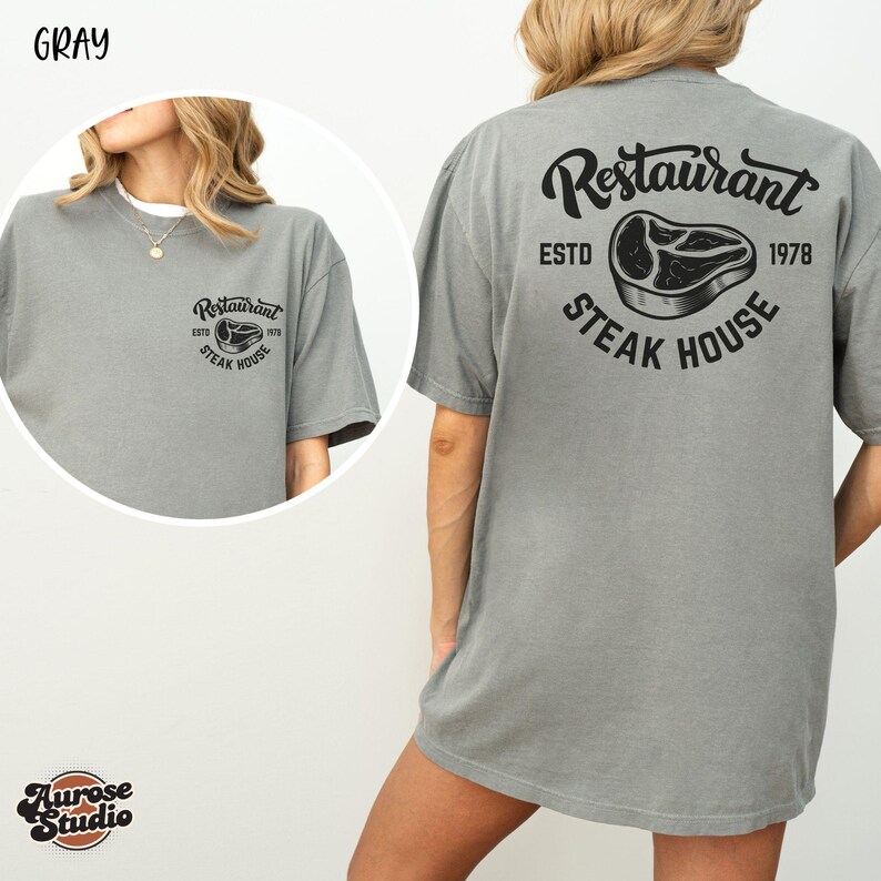 May include: Gray t-shirt with a restaurant logo on the front and back. The front logo says "Restaurant Steak House" and the back logo says "Restaurant ESTD 1978 Steak House".