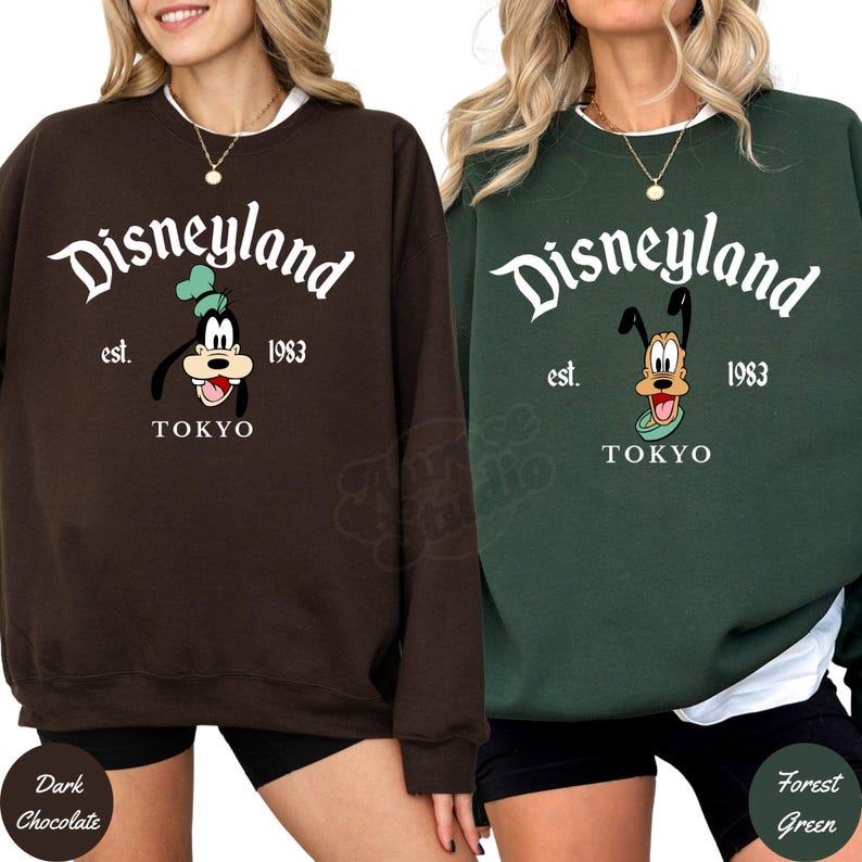 May include: Two sweatshirts, one dark chocolate and one forest green, each featuring the Disneyland logo with Goofy and the text "TOKYO" and "est. 1983". The sweatshirts have a crew neck and long sleeves.