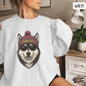 Op de afbeelding: Witte sweatshirt met een afbeelding van een lachende husky met een zonnebril en een bordeauxrode muts met de tekst "KANSAS CITY". Een comfortabele, relaxte pasvorm, geschikt voor dagelijks gebruik.